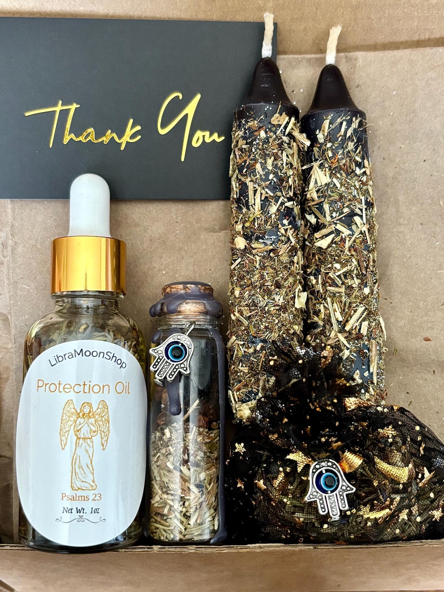 Set of 1oz. protection oil, two black protection candles dressed in herbs, glass protection spell jar with hamsa hand evil eye charm and black protection satchel with hamsa hand evil eye charm.